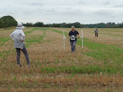 Volunteer using the geophysics survey equipment with two volunteers watching